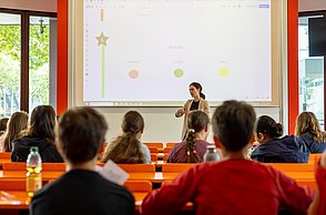 Kinder lernen Marktforschung. Professorin erklärt Fragestellungen zum Thema Eis.