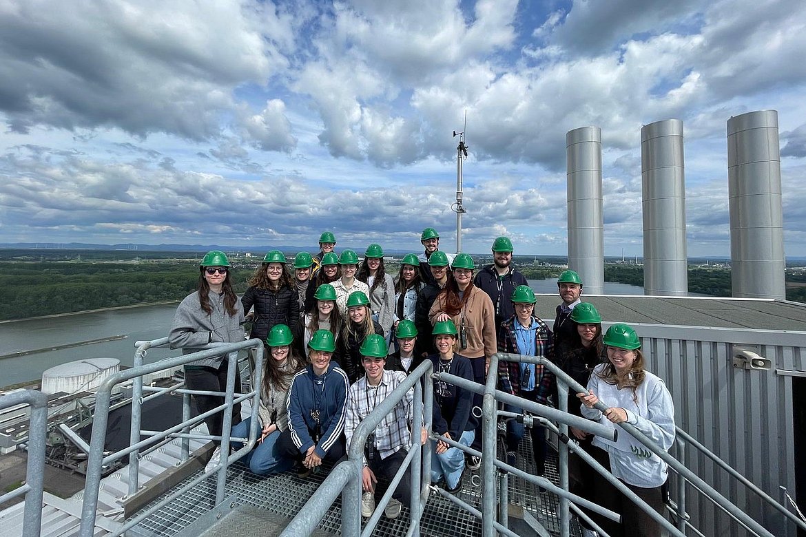 Gruppenbild mit grünen Helmen auf Dach einer Industrieanlage mit Schornsteinen