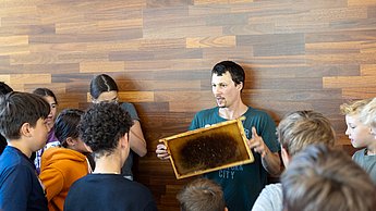 Wie entsteht eigentlich Bienenwachs? Hier zeigt Felix Bischoff den Kindern Gerätschaften dazu.