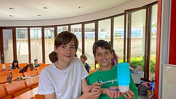 Zwei Kinder zeigen fröhlich Lampenkonstruktionen in die Kamera