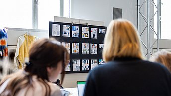 Studentinnen an einem Tisch, mit einer Pinnwand im Hintergrund