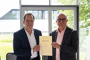 Rektor Jautz und Dr. Herpich mit der Urkunde in der Hand.