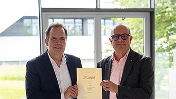 Rektor Jautz und Dr. Herpich mit der Urkunde in der Hand.