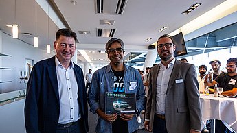 Zwei Unternehmensvertreter und ein Student mit seinem gewonnenen Gutschein