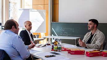 Zwei Vertreter der Firma PricewaterhouseCoopers im Austausch mit einem Studierenden