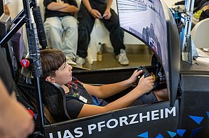Ein Kind sitzt im Rennsimulator, von hinten mit Blick auf den Bildschirm.