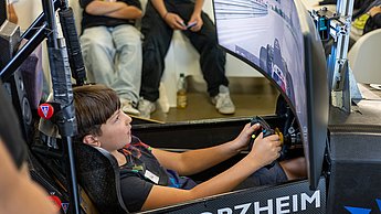 Ein Kind sitzt im Rennsimulator, von hinten mit Blick auf den Bildschirm.