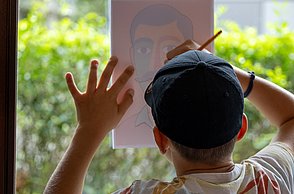 Ein Junge malt ein Bild am Fenster ab