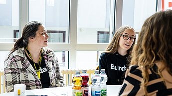 Mitarbeiterinnen der Firma Hubert Burda Media an einem Tisch mit einer Studierenden
