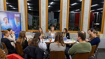 Studierende und Firmenvertreter an Tisch sitzend 
