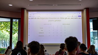Kinder lernen Marktforschung. Professorin erklärt Fragestellungen zum Thema Eis.