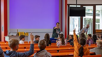 Kinder schauen sich Bienenwaben und Utensilien zur Imkerei an - hier in einer Unterrichtssituation: Kinder von hinten während Felix Bischoff vorne erklärt.
