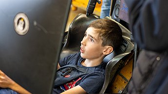 Ein Junge sitzt im Rennsimulator und schaut erschrocken, da er zu viel Gas gegeben hat und von der Bahn abgekommen ist.