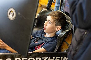 Ein Junge sitzt im Rennsimulator und schaut erschrocken, da er zu viel Gas gegeben hat und von der Bahn abgekommen ist.