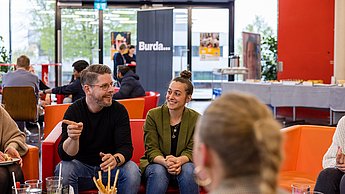 Vertreter der Firma Helmut Ruck auf einem Sofa sitzend, im Gespräch mit Studierenden