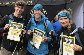 Drei Leute zeigen ihre Urkunden von einer Laufchallenge in den Bergen in die Kamera.