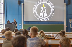 Die Kinder hatten bei der Kinderuni die Gelegenheit die Rennschmiede kennenzulernen. 3 Mitglieder stehen vorne und erklären den Kindern was genau die studentische Initiative macht.