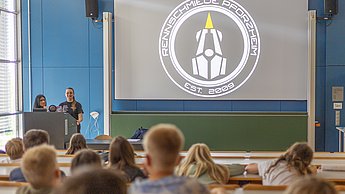 Die Kinder hatten bei der Kinderuni die Gelegenheit die Rennschmiede kennenzulernen. 3 Mitglieder stehen vorne und erklären den Kindern was genau die studentische Initiative macht.