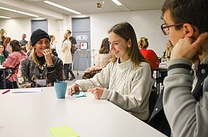 Menschen sitzen in Kleingruppen am Tisch und tauschen sich über ihre Ideen aus