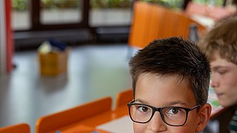 Ein Junge lächelt in die Kamera, vor ihm liegt sein halb fertiges Gesicht, das er mit Schnippseln gefertigt hat.