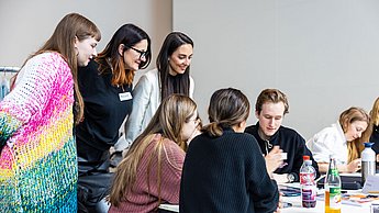 Studierende an einem Tisch und Vertreterinnen der Firma S.Oliver dahinter stehend