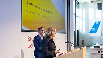 Eine Professorin und ein Professor zeigen eine Präsentation.