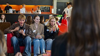 Drei Studierende sitzen auf einem Sofa und trinken Cocktails