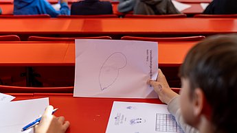 Workshopsituation: Kinder sitzen auf Plätzen und schreiben.