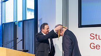 Der Rektor hängt dem Professor eine Medaille um den Hals.