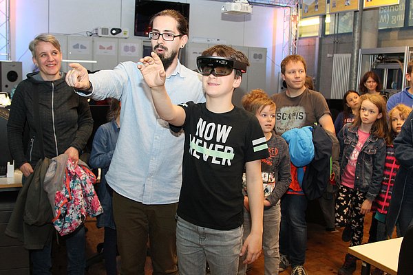 Kinder und Jugendliche bei der letzten Nacht der Wissenschaft - sie werden Betreut von einem Mitarbeiter und einer hat eine VR-Brille auf