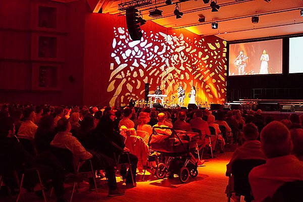 Musiker stehen auf einer festlich erleuchteten Bühne in einem vollen Saal