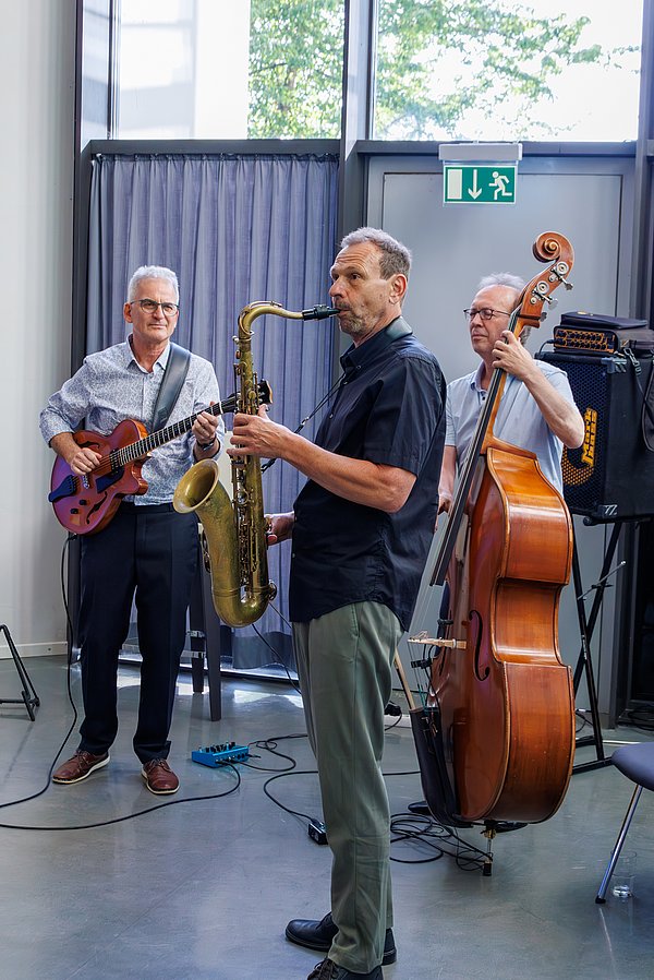 Band aus drei Männern mit Bass, Gitarre und Saxofon während eines musikalischen Stücks.