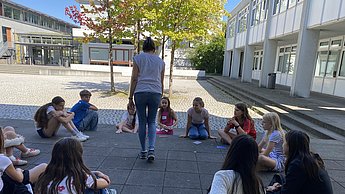 Kinder sitzen im Kreis auf dem Hof und spielen Werwolf