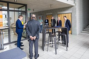 Eine Gruppe von Professoren steht um einen Tisch herum und unterhält sich.