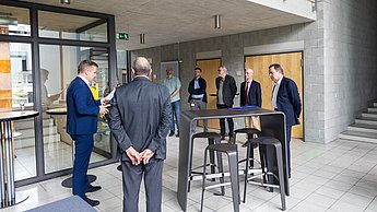 Eine Gruppe von Professoren steht um einen Tisch herum und unterhält sich.
