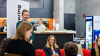 Eine Frau auf einem Sofa sitzend im Hintergrund und im Vordergrund Personen, die ihr gegenüber sitzen