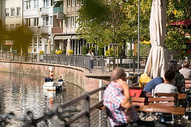 On the left-hand side you can see the Enz river, on which there is a pedalo with people. On the right, people are sitting at tables.