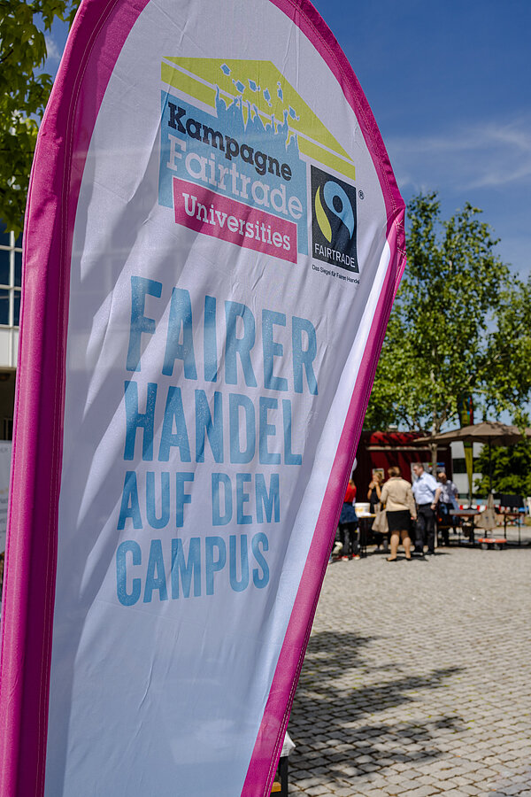 Bechflag mit Fairtrade-Uni Aufschrift, auf dem Campus stehend.