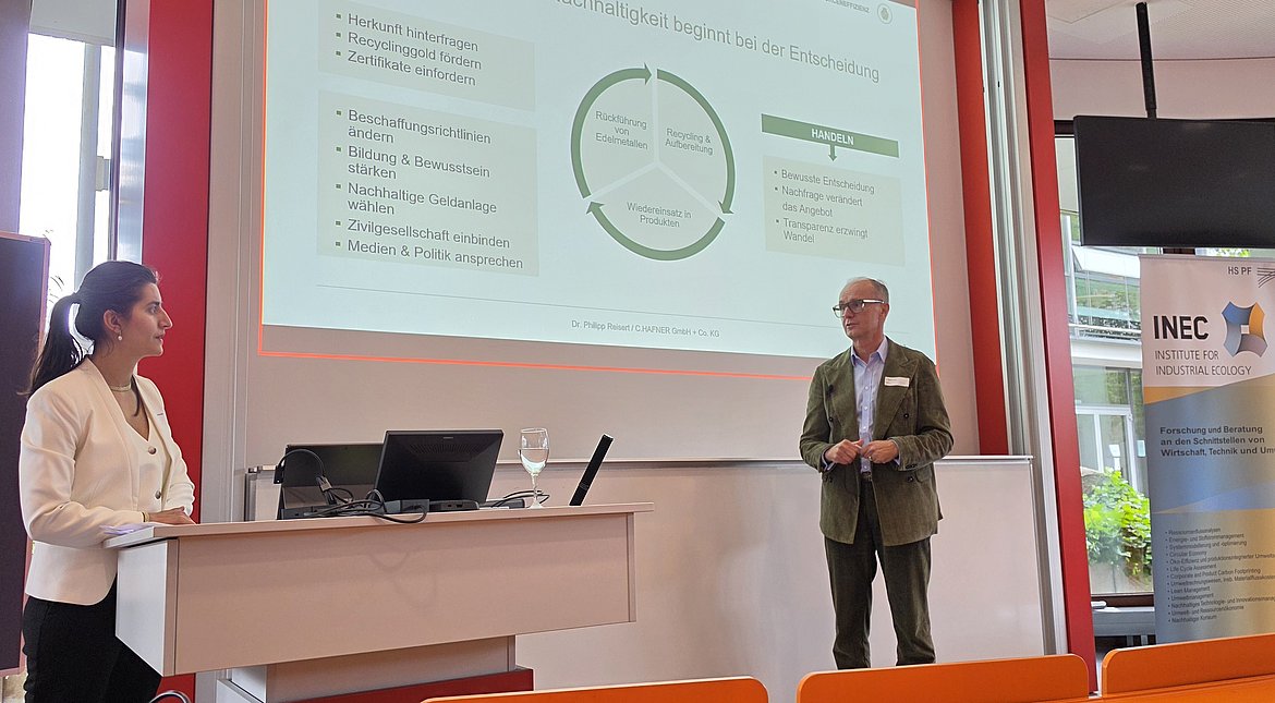 Professorin und Referent zeigen eine Präsentation.