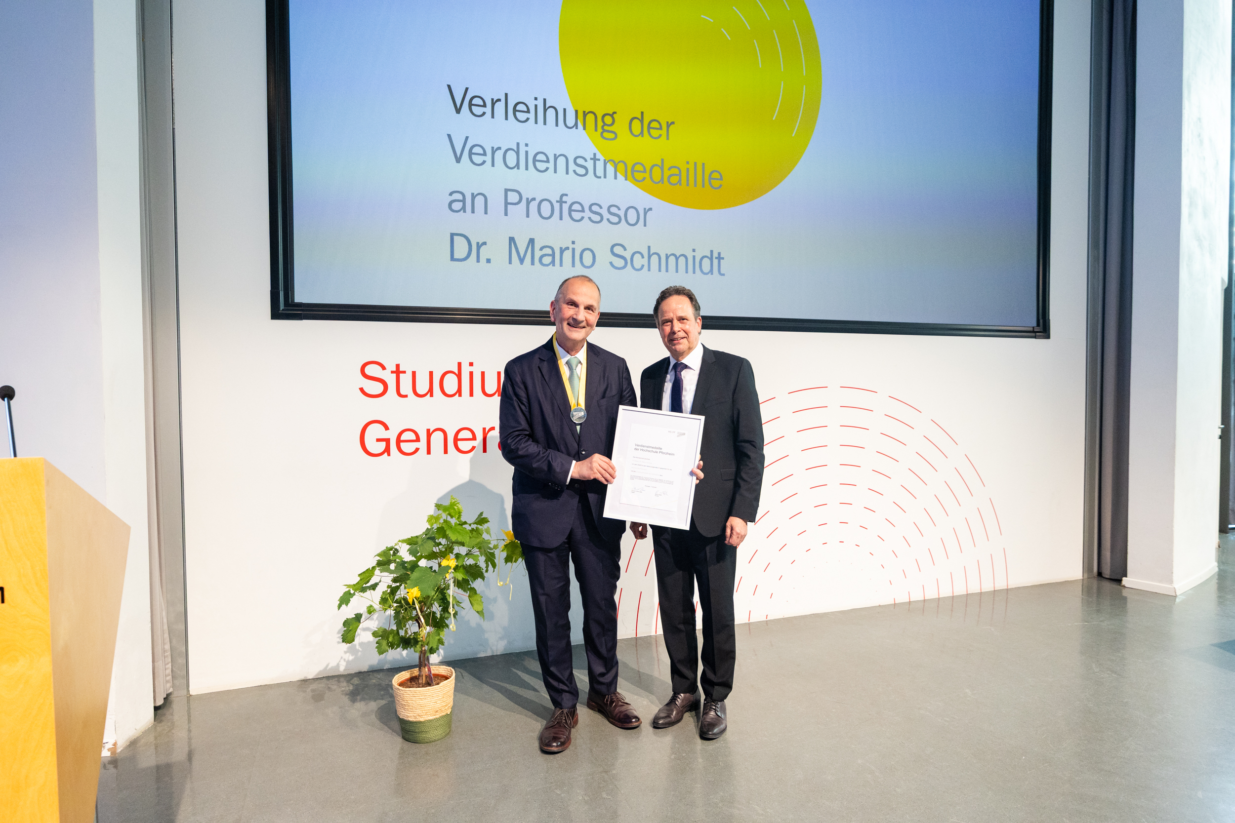Professor und Rektor halten gemeinsam eine Urkunde in der Hand.
