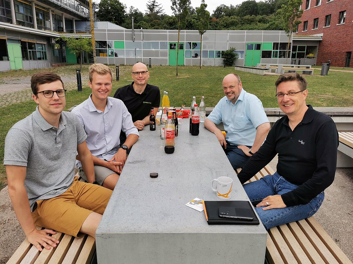 Studierende und Mentoren mit Getränken an einem Tisch.