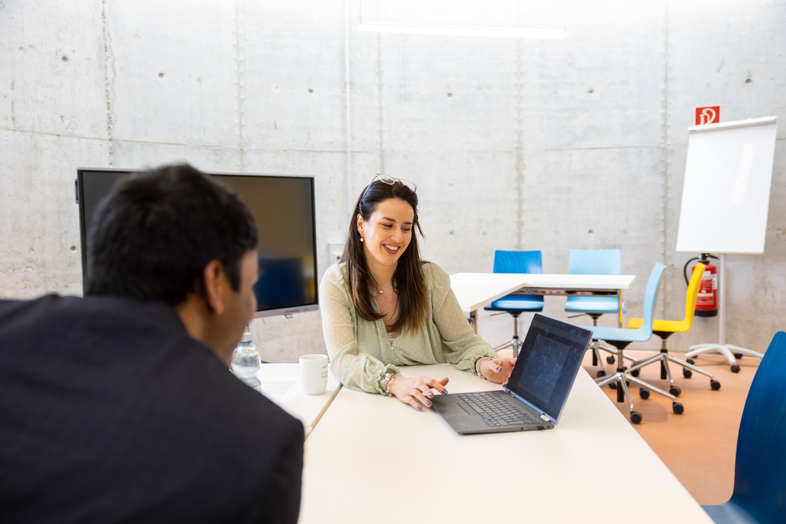 Eine Frau sitzt mit einem Studierenden an einem Tisch und unterhält sich mit ihm. 