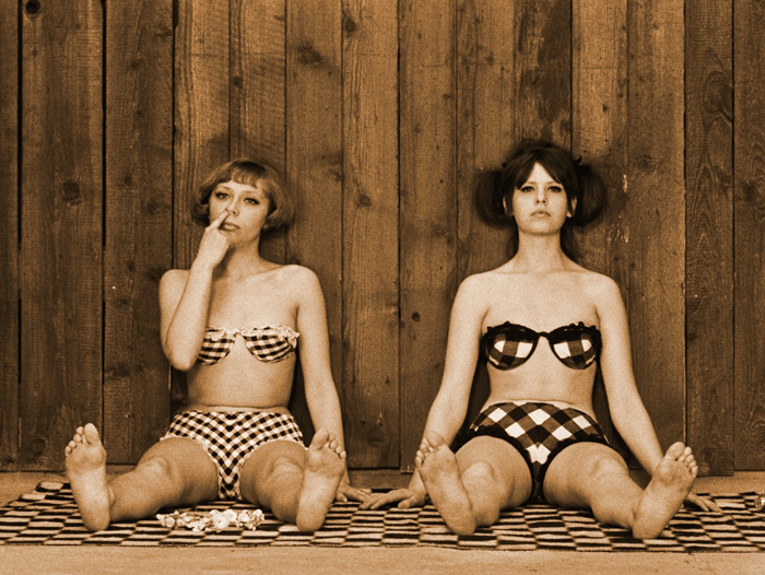 Zwei Frauen sitzen in Bikinis an eine Holzwand gelehnt.