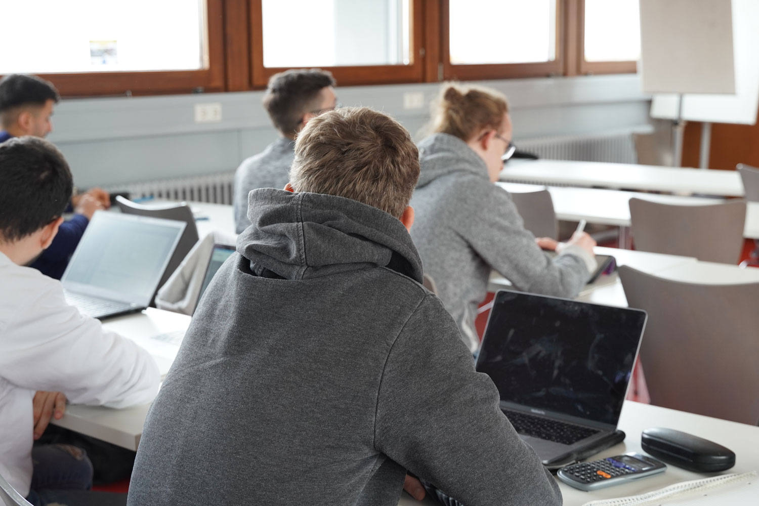A student seen from behind, seated in a university lecture hall and working on a laptop